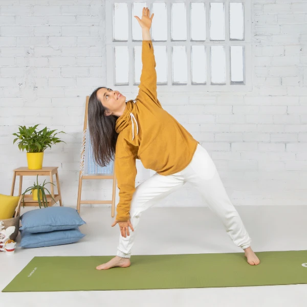 Mujer realizando la postura de Uttita Trikonasana, con piernas separadas, torso inclinado lateralmente, un brazo apuntando hacia el pie y otro hacia el techo.