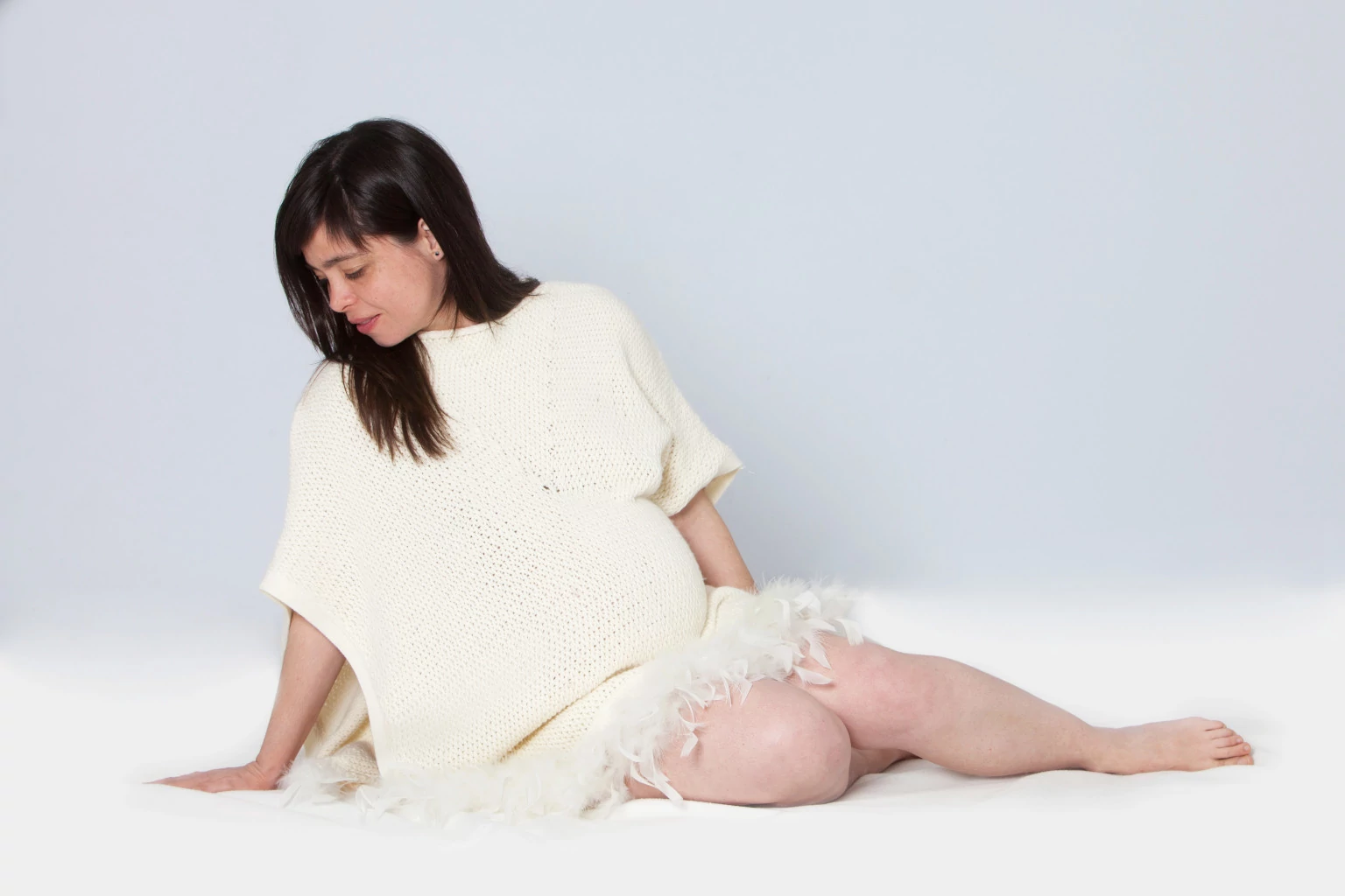 Mujer embarazada sentada con poncho de plumas