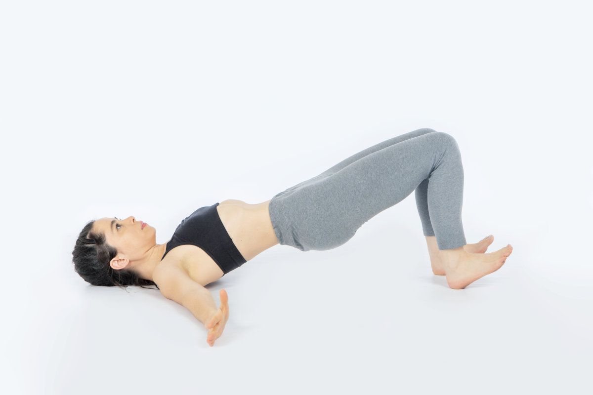 postura afrodita hipopresivos low pressure fitness – Shivalans Mujer tumbada boca arriba en postura de Afrodita de Low Pressure Fitness, con rodillas flexionadas, tobillos en dorsiflexión y brazos cerca de caderas